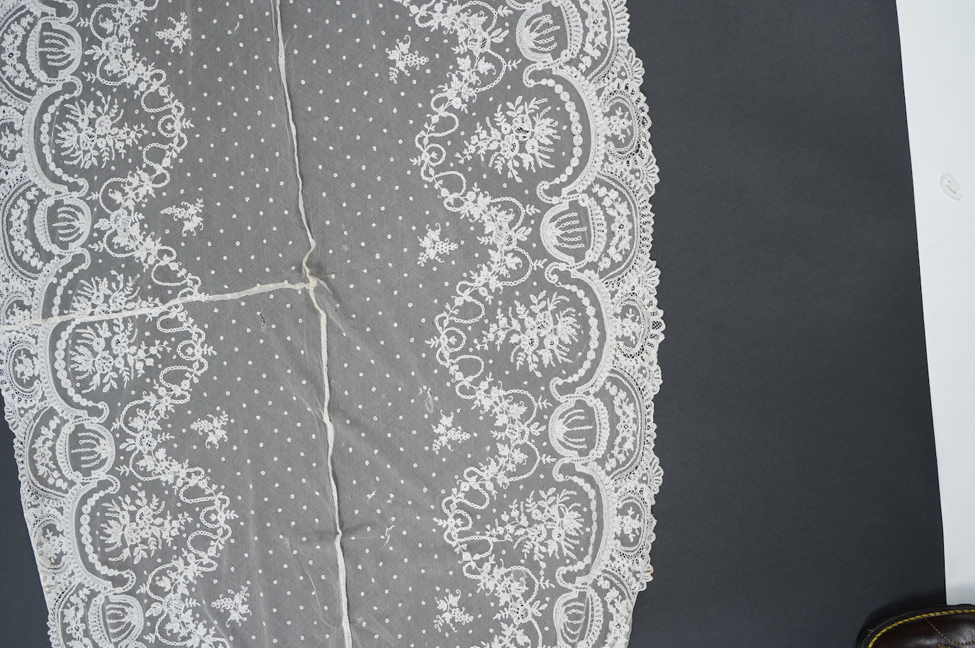 A wide flounce of fine ornate hand made 19th century Brussels bobbin lace, appliquéd onto a net ground, possibly commissioned for a wedding gown, now sewn together along the top edge and the two cut ends also stitched to